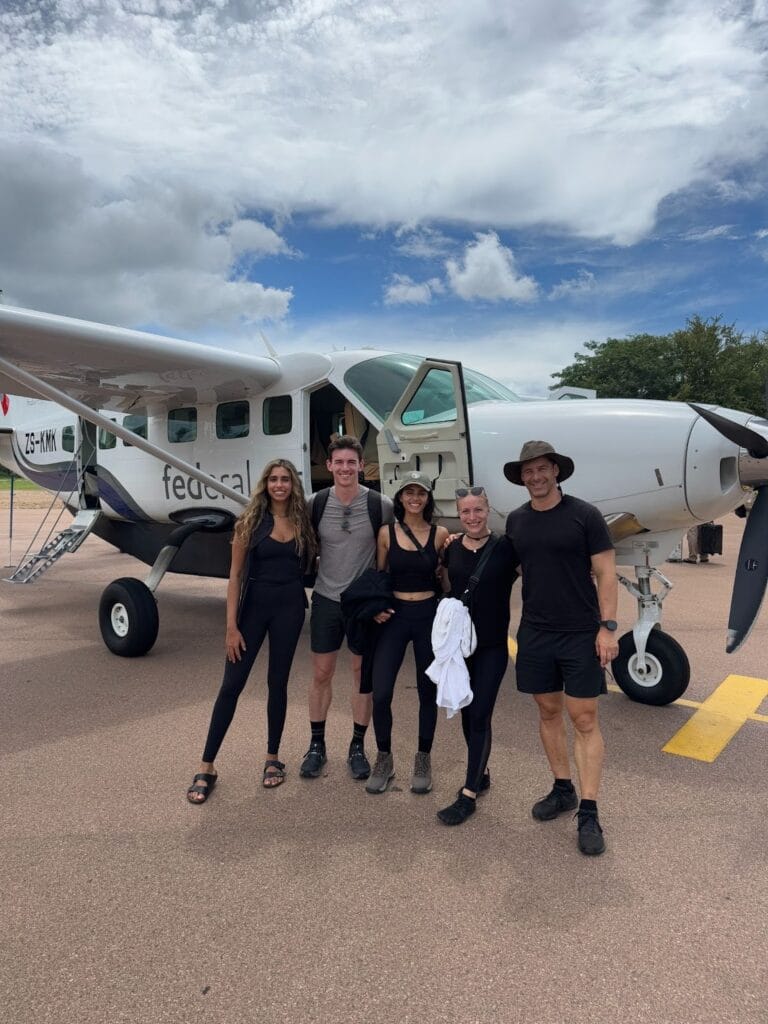 Five travelers posing in front of a small bush plane on an airstrip during a South Africa safari trip