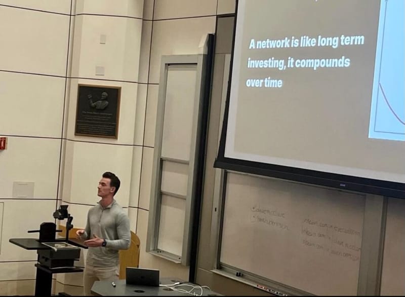 Noah Berkson presenting at a lectern beside a slide that reads 'A network is like long term investing, it compounds over time'