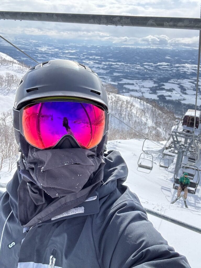 A selfie in a ski helmet and mirrored goggles on a gondola above a snow covered mountain valley in Japan